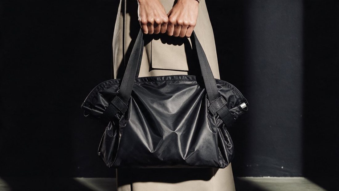 Le sac fourre-tout KUZALI en tissu Oxford noir, tenu à la main sous une lumière rasante
